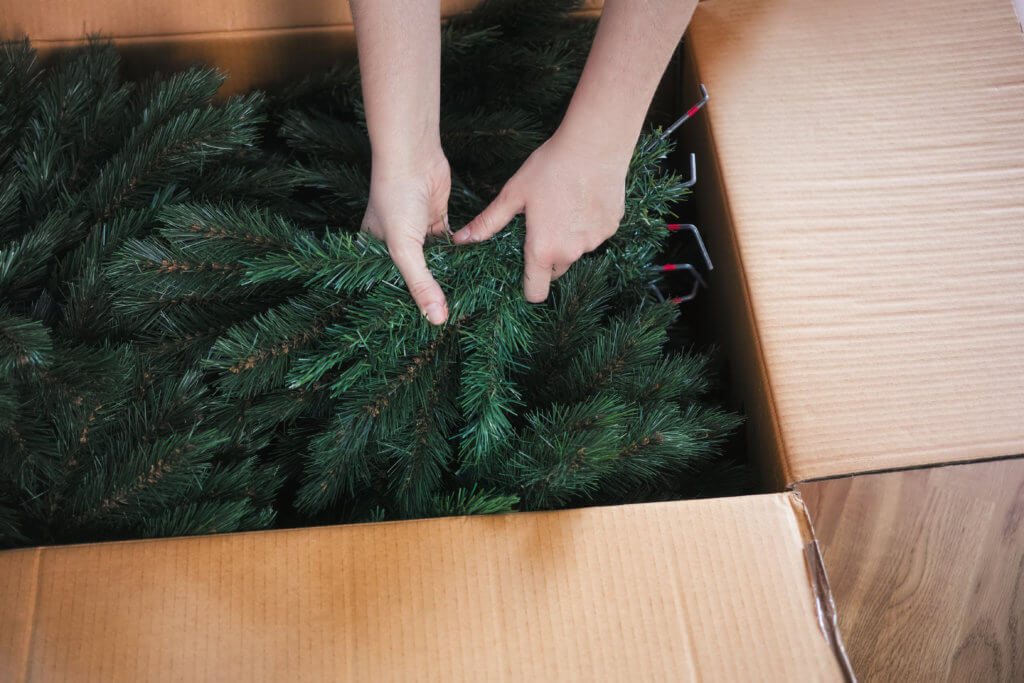 Woman hands taking an artificial Christmas tree branches out of a large cardboard box